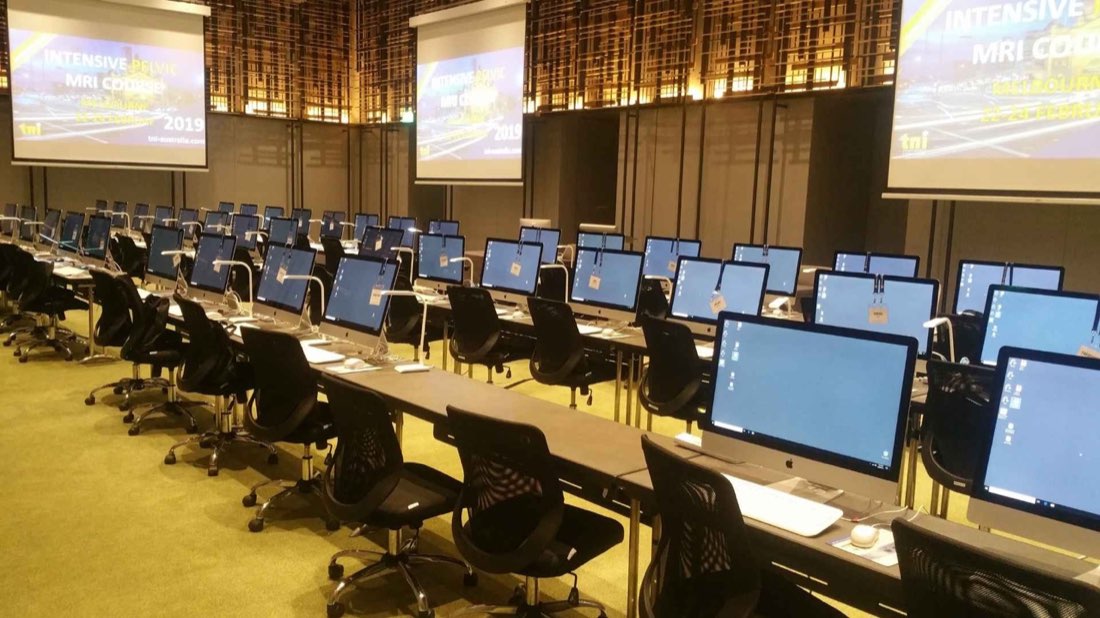 Rows of workstations and projector screens supplied by Hire Intelligence at a large training event